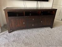Front view of dark stained wood TV console showing two doors, two drawers, and open shelves under television.