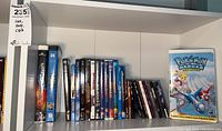 Shelf showing multiple DVDs and VHS including Pokemon Heroes The Movie VHS
