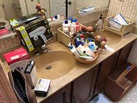 Photo showing bathroom counter with Conair hairdryer box, Omron wrist blood pressure monitor box, digital scale, plastic basket containing bath products, and pill cases in the background.