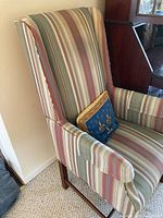 Full view of upholstered wingback chair with striped fabric upholstery and wooden legs