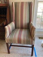 Front view of the wing chair showing vertical multicolor stripes upholstery and wooden legs.