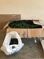 Box containing disassembled artificial Frasier Fir tree sections and separated string lights in a plastic bag.