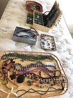 Costume jewelry laid out on light-colored fabric including multiple necklaces and trays with assorted pieces.