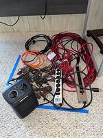 Multiple extension cords in red, orange, black, brown colors, two power strips and small black Pelonis heater with dials on carpet