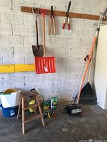 Full lot overview showing garden tools, ladder, battery charger, buckets, plant food in a garage setting