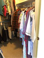 Wide view of closet showing multiple jackets, coats, suits, and dresses hung on hangers