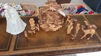 Full view of nativity set including stable, multiple wood carved figures such as animals and humans, and the white ceramic figurine placed to the side.
