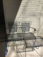 Angled top-front view of metal patio bench and side table showing the mesh and scrollwork details on both pieces.