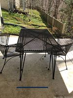 Metal patio furniture set including rectangular table and two chairs on outdoor patio.