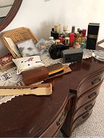 View of perfume bottles along with other personal items on wooden dresser with lace doily.