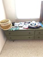 Three woven baskets, folded scarves, and winter accessories on a green dresser in natural light.