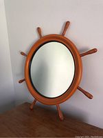 Front view of the ships wheel mirror hanging on a wall showing its full round wooden frame and eight handles.