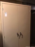 Front view of the beige metal two-door storage cabinet showing locking handles and intact surface.