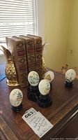 Set of three vintage hardcover books titled 'Stevenson's Works' between two gold-colored pineapple bookends showcasing the spine and side edges of books, with six Asian painted decorative eggs on black stands arranged in front.