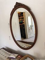 Full view of the oval wooden mirror hung on a wall with visible carved decorative top.