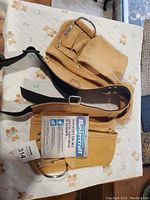 Photo of new, unused Mastercraft carpenters tool belt made of tan suede leather, with multiple pockets and metal rings, laid out on a light-colored surface with bear print.