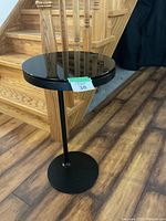 Front view of round black Ikea end table with metal column and circular base, dark glass top reflecting surroundings.