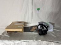 Photo of the headphones out of the box with the original packaging, manual, and charging cable visible.