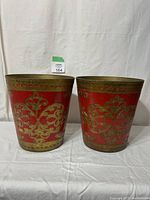 Front view of both vintage Florentine plastic waste baskets showing red color and ornate gold decorations.