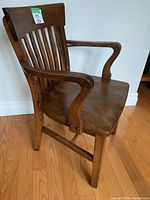 Angled side view of solid wood vintage office chair, showing curved armrest, slatted backrest, contoured seat, and wood grain finish.