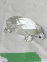 Swarovski crystal turtle figurine on light fabric background, showing faceted body and legs with black eyes detail.