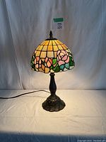 Frontal photo of Tiffany style lamp lit showcasing its warm stained glass floral shade and decorative metal base.