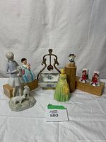 Full view of various ceramic statues and items including figurines of girls, animals, and a decorative ceramic container with metal handle.