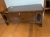 Front and side view of walnut cedar chest showing carved details, black oval insets, and bracket feet.
