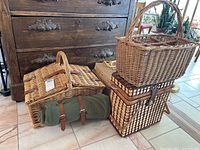 Four wicker picnic baskets stacked and arranged on floor near dark wooden chest and chair