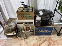 Overview of the lot showing canning jars in cardboard box, wooden kitchen utensils, metal chinois strainer, and large black enamel stock pot with lid