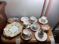 Full view of four sets of teacups and saucers, small decorated plates, a floral vase on a plate, and other assorted fine china pieces arranged on wooden small table