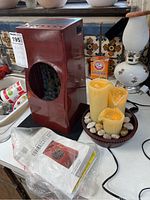 Rectangular wooden indoor water fountain with circular front opening revealing multicolored stones and cascading water, alongside LED lighted candles in a round bowl with decorative white rocks.