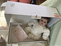 Vinyl baby doll lying in white box with birth certificate beside it