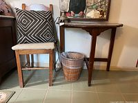 Wooden side chair with cloth seat cushion and black and white geometric throw pillow next to wooden demi lune table.