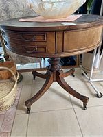 Photo showing front view of oval wooden game table with curved legs and drawer on antique metal casters.
