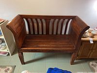 Front view of entire wooden bench showing high back, slatted seat and carved apron.