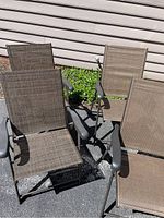 Four outdoor folding chairs outside with two different mesh patterns: two with plain woven fabric and two with checkered woven fabric, all brown.
