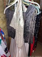 Six ballroom dresses hanging on plastic hangers in a closet, showing a variety of styles and sequin decorations.