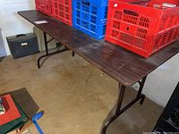 Full view of the banquet folding table showing dark wood-tone surface and metal legs with floor and wall background.