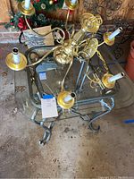 Photo showing the brass toned chandelier placed on top of the glass top end table, displaying chandelier detail and table size.