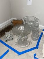 Photo shows all items in the lot on a carpeted floor: a large glass ice bucket with handles, two decorative glass bowls, a wine decanter, oil and vinegar set on tray, and Waterford teddy-shaped clock.