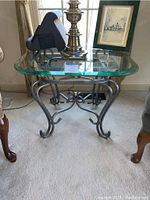 Front view of metal base glass top end table with lamp and decor on top, showing curved legs and scrollwork on the base.