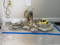 Overview of various hand-painted china including stacked plates, serving bowl, and tall pitcher (pitcher excluded from sale).
