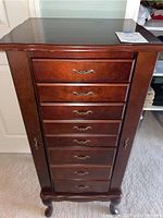 Front view of the wooden standing jewelry armoire showing eight drawers and side doors closed.
