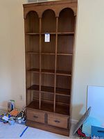 Front view of tall stained wood bookshelf with a drawer at the bottom, showing three shelf sections and decorative arch molding.