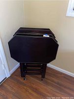 Four stacked dark wood TV tables with octagonal tops and a matching stand beneath them.