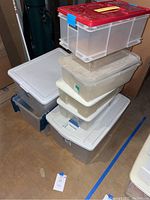 Stacked clear plastic storage containers, various sizes, with matching lids, one red lid with blue clips on top