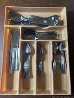 Photo of the flatware organized by type in a sectioned drawer organizer showing knives, forks, spoons, serving utensils.