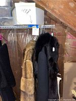 Faux fur and black fur coats hanging on rack in attic space.