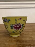 Side view of the antique Chinese porcelain cup showing floral design on yellow background and minor chip on rim.
